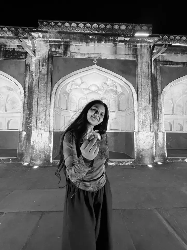 Bhumika at an old stone gateway in the evening, holding a flower